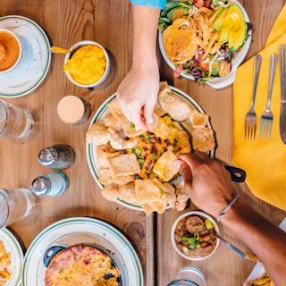 Top-down view of a table filled with food with two hands reaching for items on the table.