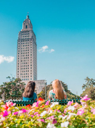 two ladies sitting on a bench with the Louisiana state capitol in the background