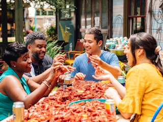 A group of four people enjoying a lively seafood feast, sharing crawfish at a vibrant outdoor table surrounded by greenery.