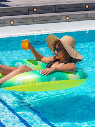 Woman wearing a hat and sunglasses enjoys a drink while floating on a tube in a pool in Baton Rouge