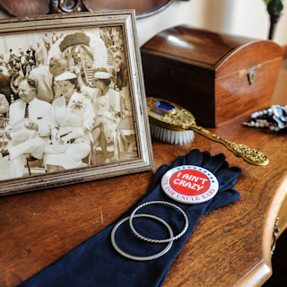 A vintage framed photograph sits on a wooden table at the Old Governor’s Mansion, accompanied by a black glove, campaign button, decorative brush, and jewelry.