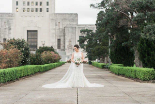 A bride in a white dress standing in front of a gray building